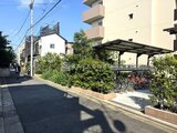 クレアティフ三軒茶屋 緑に囲まれた駐輪場と建物外観を前面道路から見た様子
