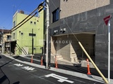 ラグゼナ北千住2 建築中の駐車場入口と隣接する黄色い建物の外観