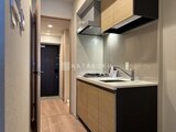 リビオメゾン浅草雷門 モダンで落ち着いた色合いのキッチン、玄関への廊下から見た様子