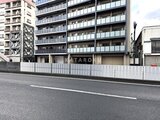 アリビス五反野 前面道路から見たモダンな外観の建物と白いフェンス