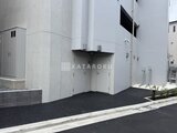 ジェノヴィア北千住 白いコンクリート造の建物とアスファルト舗装された駐車スペース