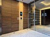 コンシェリア町屋 エレベーターホールで、木目調パネルと間接照明が落ち着いた雰囲