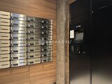 コンシェリア町屋 木目調パネルに並ぶメールボックスと管理用の黒いパネル