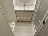 コンフォリア・リヴ押上ノース 白い洗面台と木目調の収納が備わった清潔感のあるトイレ空間