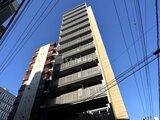 ブリリアイスト御茶ノ水 青空を背景に見上げた建物外観と隣接する低層建物の様子