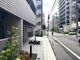 クラリティア上野稲荷町 植栽の緑が映えるモダンなエントランスと街並みの様子