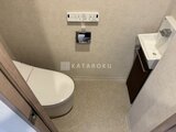 プライムブリス森下スタジオ 温かみのあるトイレ空間に温水洗浄便座と手洗いが備わった様子