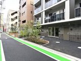 コンフォリア・リヴ文京千駄木 緑のラインが特徴的なアプローチから見たモダンな建物外観と植栽