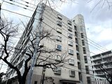 コンフォリア高島平 街路樹とビル群が立ち並ぶ前面道路から見た建物外観