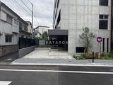 ジェノヴィア竹ノ塚 前面道路から見たモダンなコンクリート造の建物外観と駐車場入口
