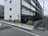 ジェノヴィア竹ノ塚 前面道路から見たモダンな外観と黒いフェンスで囲まれた駐車場