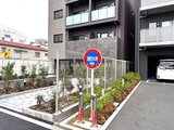アルコバレーノ南千住 駐車場の看板が立つモダンな建物の外観と植栽のある敷地の様子