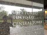 シティタワーズ東京ベイ 建物の外壁に施された物件名と棟名の表示と背景の緑が見える様子
